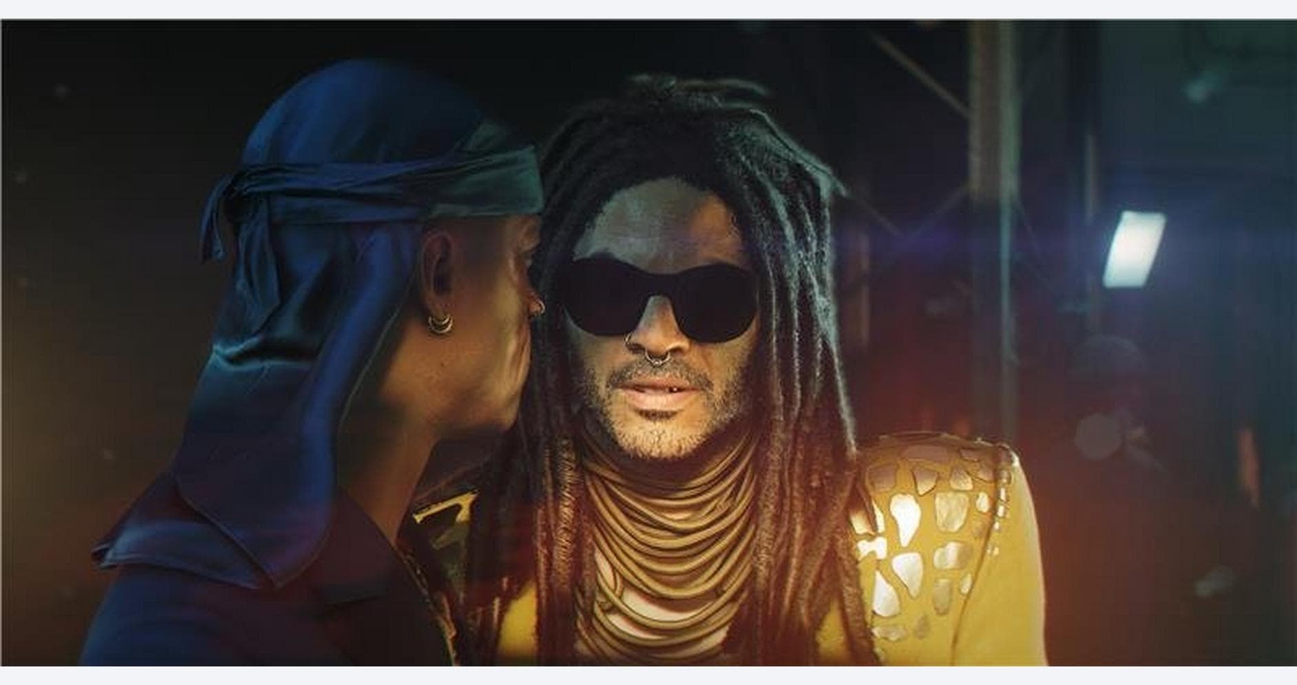 Two characters in a tense conversation, one with dreadlocks and sunglasses, in a dark setting.