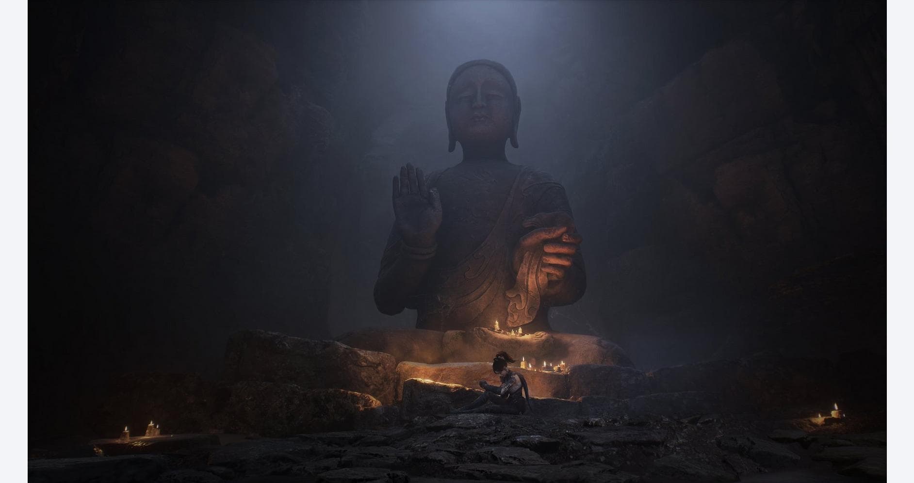 Large Buddha statue in a dark, misty environment with candles and a person sitting nearby.