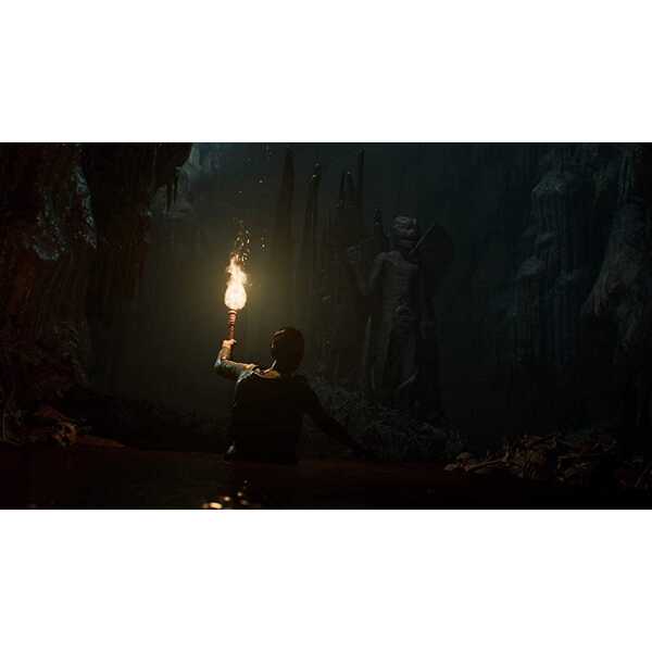 Person holding torch exploring dark cave with mysterious statues.