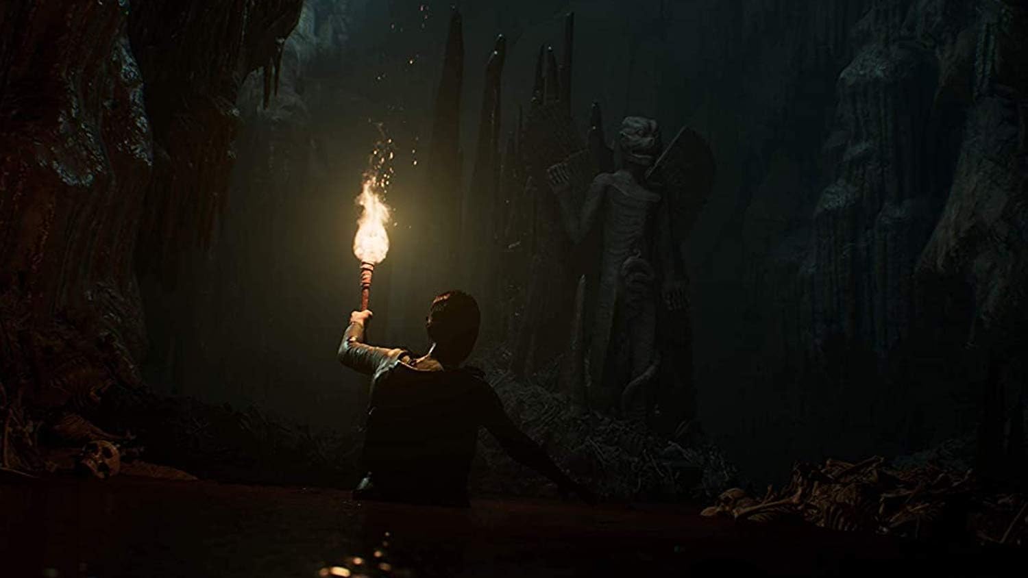 Person holding torch exploring dark cave with mysterious statues.