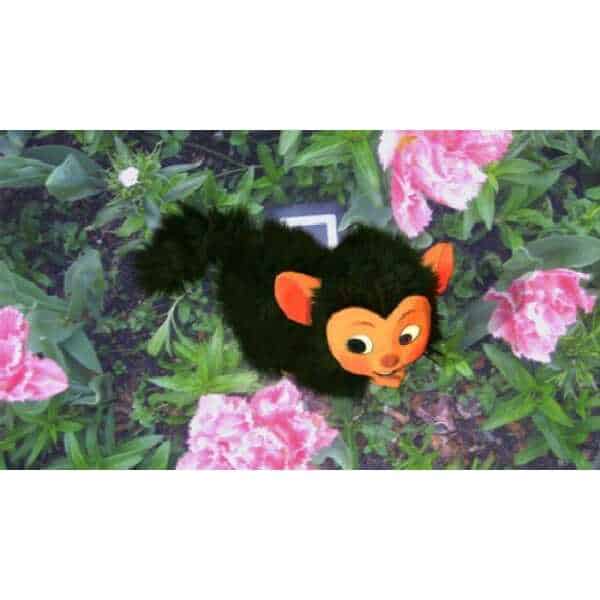 Cute plush toy of a monkey with black fur and orange face among pink flowers.