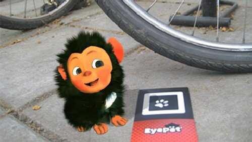 Cute virtual pet monkey from EyePet game on a sidewalk with a bike wheel nearby.