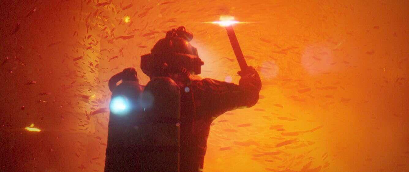 Diver holding a torch in a fiery, underwater scene with orange hues.