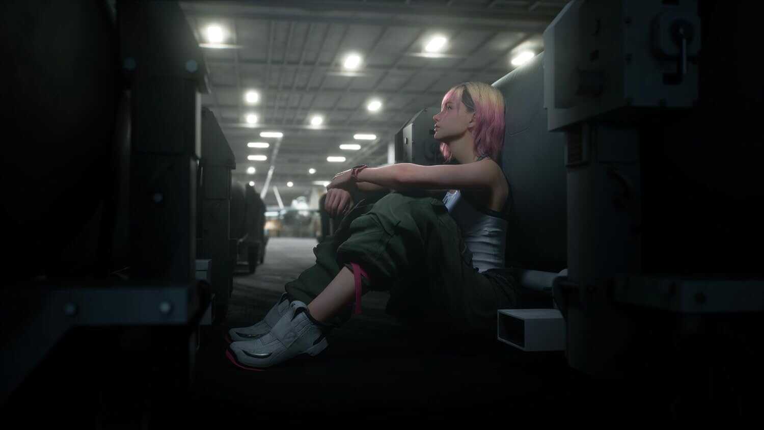Young woman with pink hair sitting on the floor in a parking garage at night.