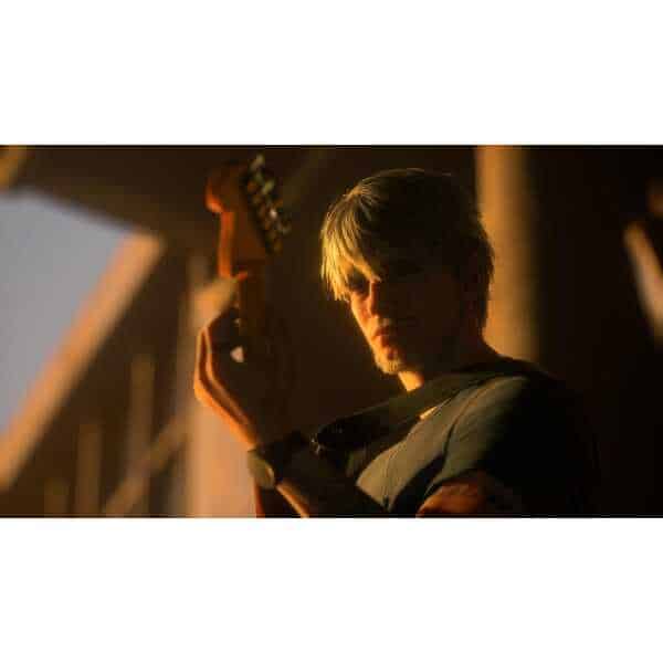Young man playing electric guitar in warm, low-light setting.