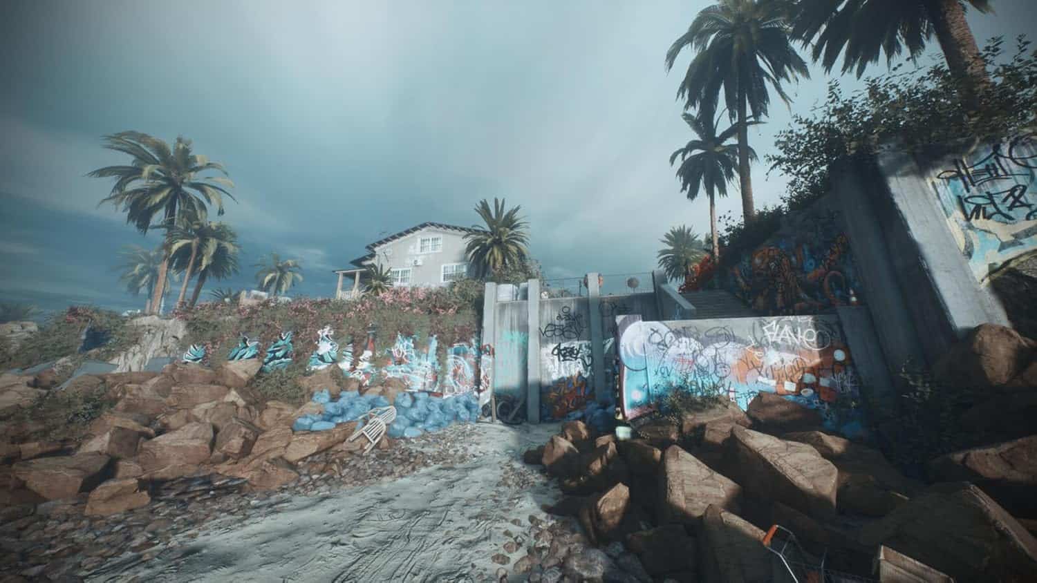 Urban scene with graffiti, rocks, and palm trees under cloudy sky.