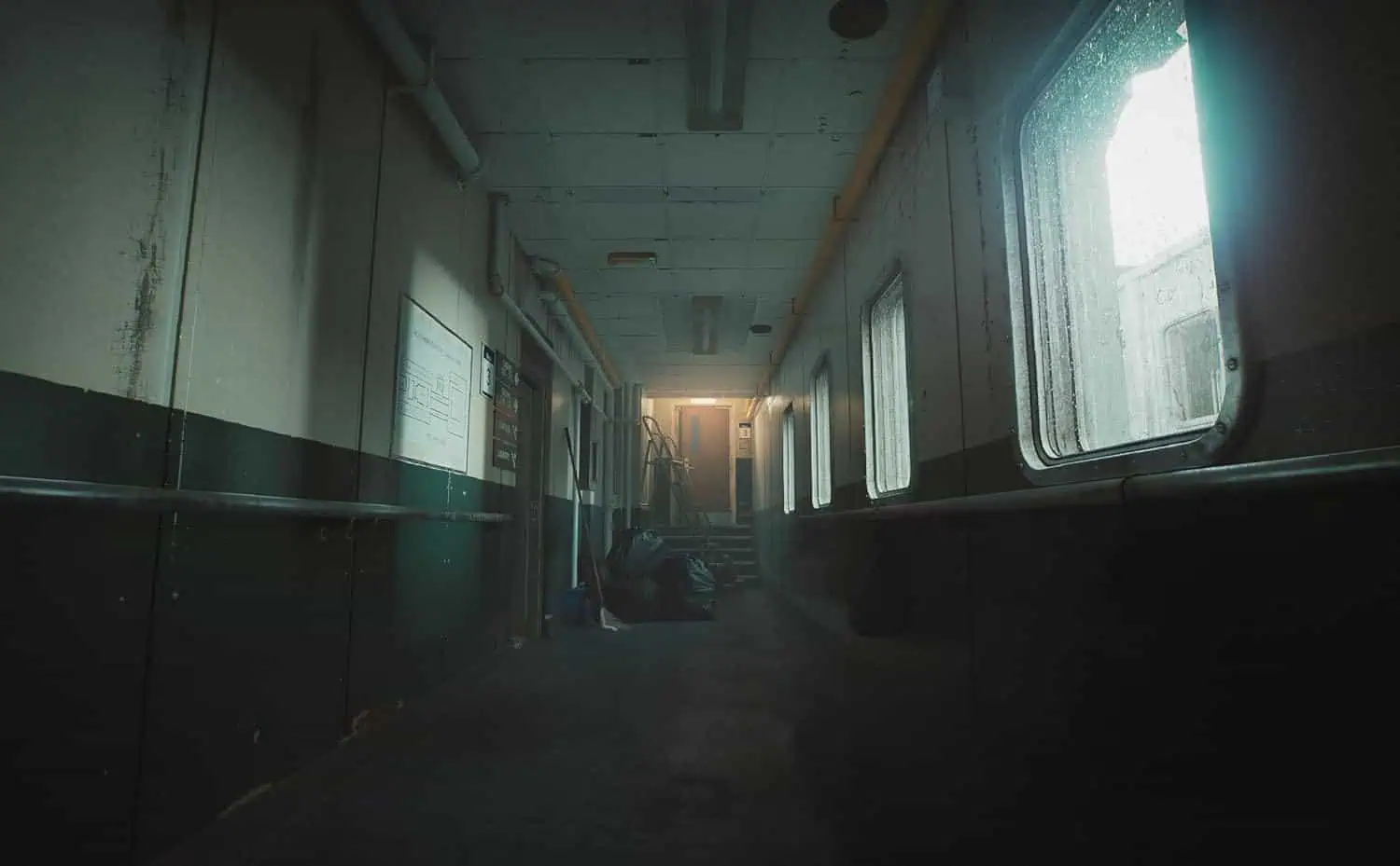 Abandoned industrial corridor with dim lighting and foggy atmosphere.