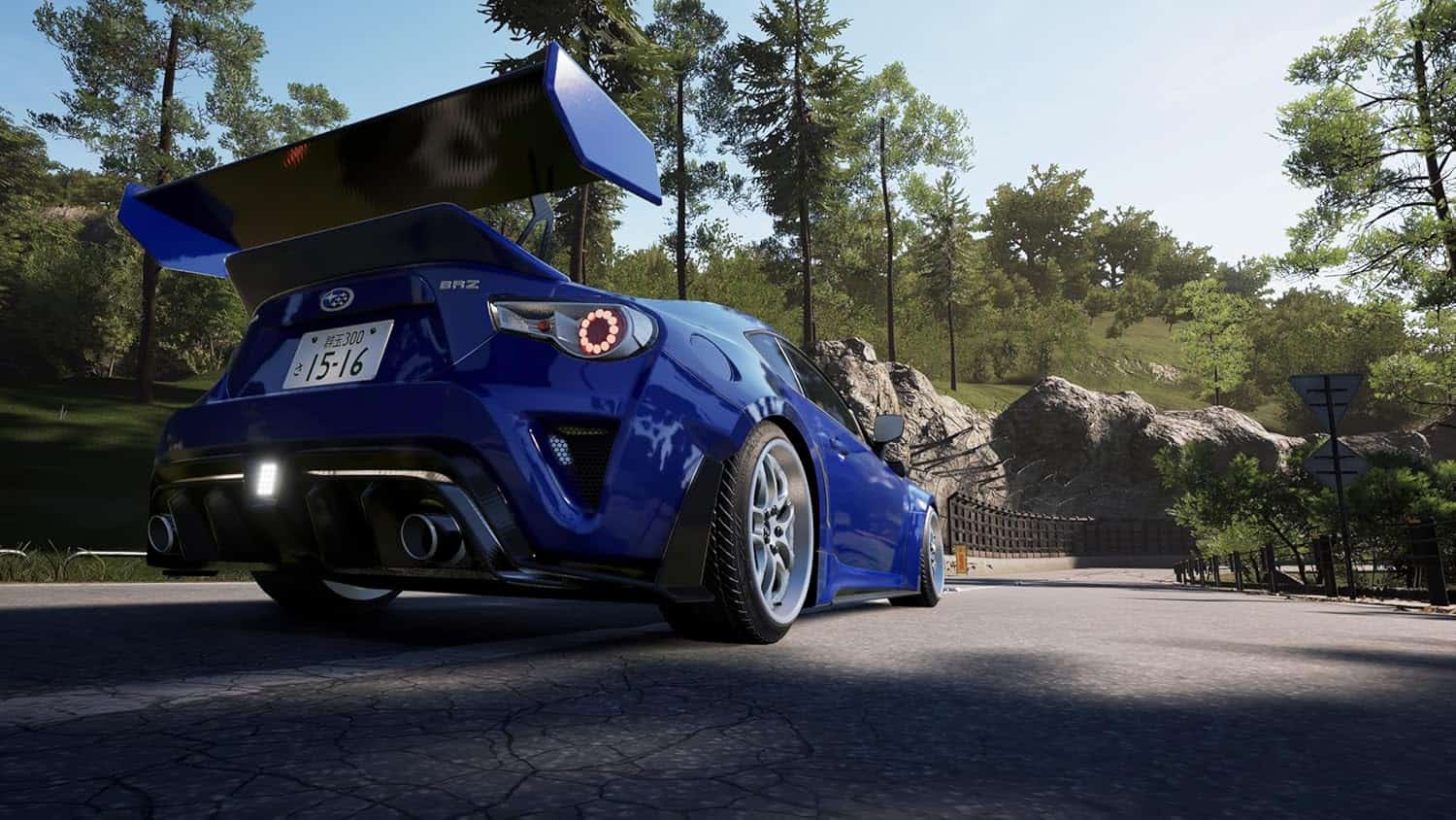 Blue racing car with large rear wing on scenic road, showcasing high-performance vehicle.