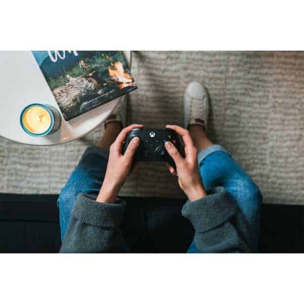 Person playing video games with a game controller on a cozy carpeted floor.