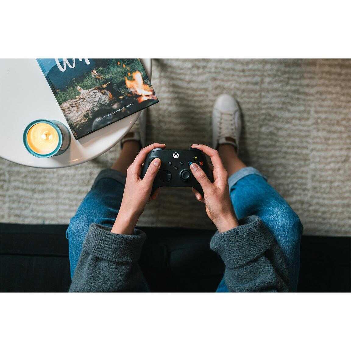 Person playing video games with a game controller on a cozy carpeted floor.