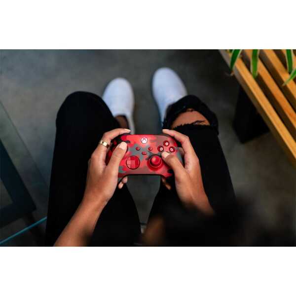 Person holding a red gaming controller with black buttons and thumbsticks.